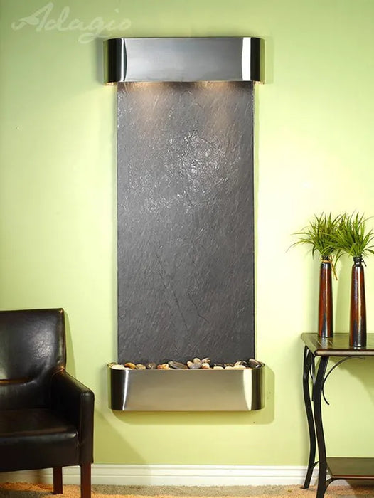 Wall-mounted water feature with dark stone finish and metallic frame against a light green wall.