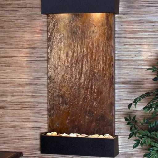 Decorative indoor wall fountain by adagio water feature with textured metal panel and black base against a wooden wall.