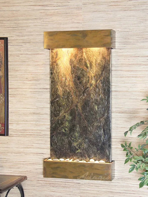 Decorative in door wall fountain by adagio water features with marble-like design and brass accents on a light wood paneled wall.