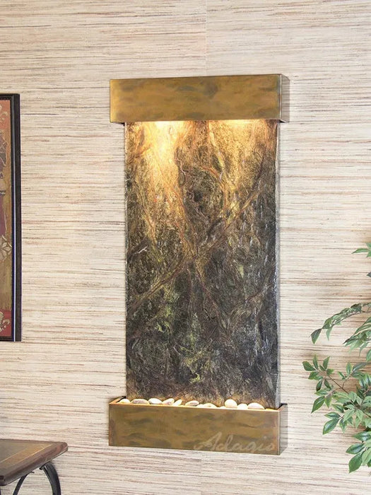 Decorative in door wall fountain by adagio water features with marble-like design and brass accents on a light wood paneled wall.