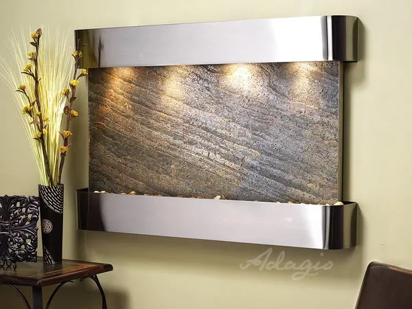 Wall-mounted water feature with metallic finish and decorative elements on a beige wall.