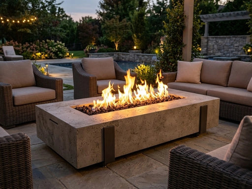 American Fyre Designs Basalt 72 inch fire table illuminated at dusk on a stone patio with active linear flame output surrounded by outdoor lounge seating