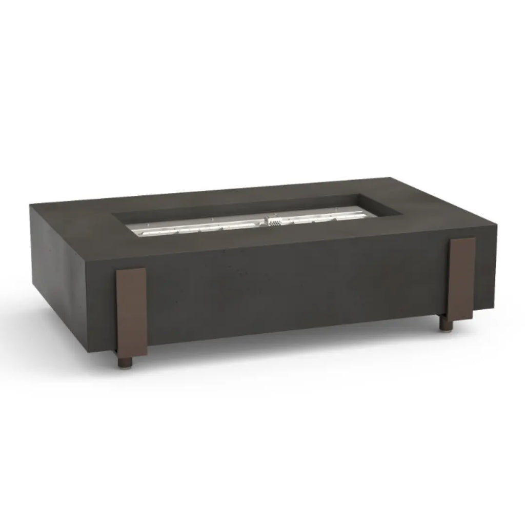 A dark gray rectangular fire table made of concrete with bronze-colored metal accents on the sides, featuring a long, rectangular stainless steel burner in the center.