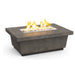 A rectangular fire pit table with a gray concrete-like finish. The table has a stainless steel burner tray with white fire glass and a dancing flame visible.