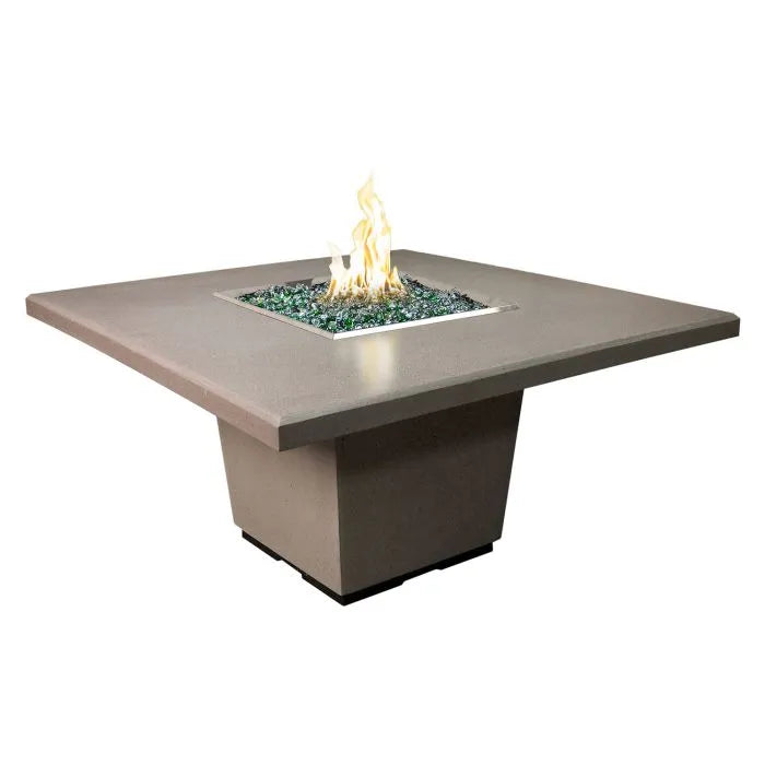 A photo of the American Fyre Designs 60" Cosmopolitan Square Dining Fire Pit Table, showcasing its square shape, light-colored concrete finish, and a warm, inviting fire burning in the center.