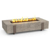 A light gray rectangular concrete fire table with a central burner showing flames, and bronze-colored metal accents on the sides.