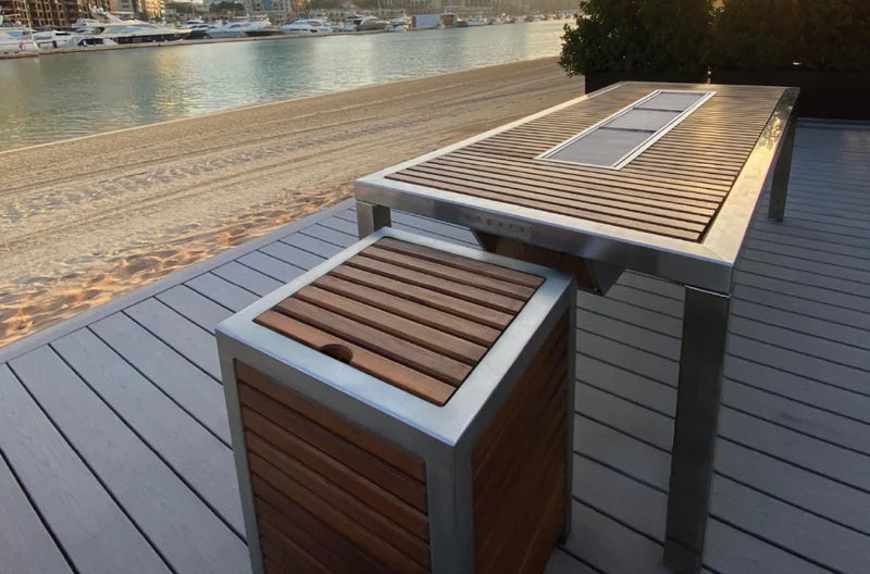 Wooden outdoor knorean grill table and bench set on a deck by a waterfront.