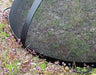 A close-up of the bottom edge of a black metal spark guard. The spark guard is resting on a bed of purple flowers.