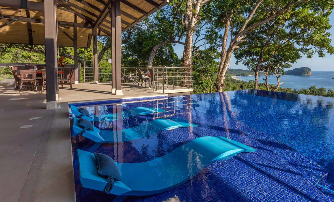 A photo of a large infinity pool with blue water and blue floating loungers.