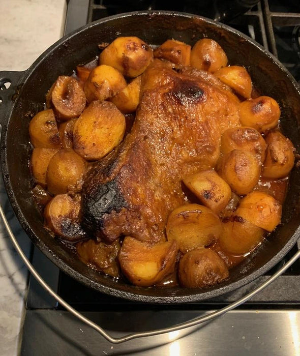 A cast iron Dutch oven filled with a roasted beef brisket and golden potatoes. The meat is browned and glazed, and the potatoes are tender and slightly caramelized. The dish is sitting on a stovetop.