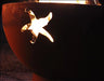 A close-up of a starfish cutout in a round, rusted metal fire pit. Flames are visible through the cutout.