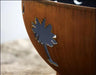 A close-up of a palm tree cutout in a rust-colored fire pit. The cutout is filled with shadow, creating a contrast against the warm metal.