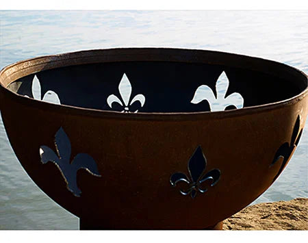 A close-up of a round, rust-colored fire pit with fleur-de-lis cutouts. The cutouts are filled with white light, creating a contrast against the dark background.