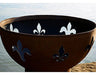 A close-up of a round, rust-colored fire pit with fleur-de-lis cutouts. The cutouts are filled with white light, creating a contrast against the dark background.