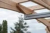 A close-up of the corner of a wooden pergola, showing the intersection of a beam and a post. The beam is secured with screws and brackets.