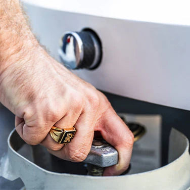 Close-up of a hand adjusting the control knob on a fire pit, with a focus on the hand and the knob.