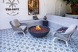 Outdoor seating area with a fire pit, chairs, and decorative elements on a patterned floor.