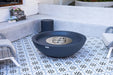 dark gray fire pit table on a patterned patio with chairs and decorative elements.