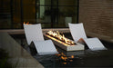 Two white modern lounge chairs partially submerged in a pool, flanking a rectangular fire pit with a visible flame.