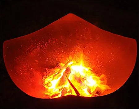 A close-up of a fire pit with flames burning inside. The fire pit is glowing orange, and the flames are casting a warm light on the surrounding area.