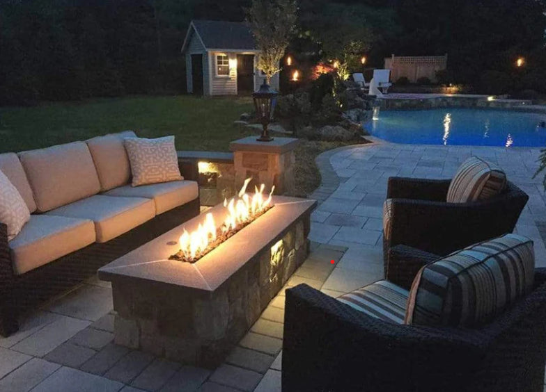 A wooden bench with a slatted back and seat sits on a stone patio. A round wooden table with a pedestal base complements the bench.