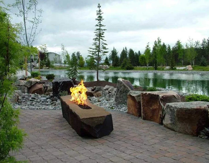 A fire pit made out of a large rock. The fire pit has a rough, natural look and is surrounded by pebbles.