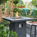 dark grey square bar height fire pit table is lit on lava rocks and has square glass windscreen around it outside USA bar