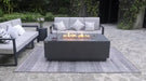 dark grey luxury fire table has a fire lit in the middle. fire table is placed on top of a rug in the middle of sofas