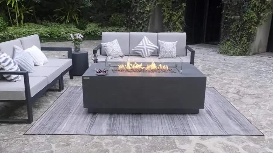 Contemporary gray fire table with glass surround, surrounded by a gray sofa and loveseat on a patio.