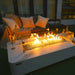 rectangle fire pit table with glass guard. fire pit is lit with bright yellow and orange flames with wine glass on the table in outdoor patio setting