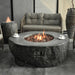 elementi boulder rock fire pit OFG110. it is in high performance concrete material. there is 2 cups of coffee on top of the fire table. the fire pit is also lit on rocks with a big flame