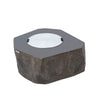 A large, round, concrete fire pit with a textured, rock-like finish. The fire pit has a central bowl with a white cover over it.