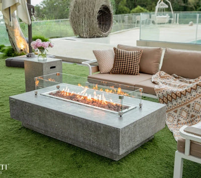 Elementi Hampton light grey rectangular fire pit coffee table with glass surround. flames are lit and burning on a bed of red lava rocks in outdoor patio. 