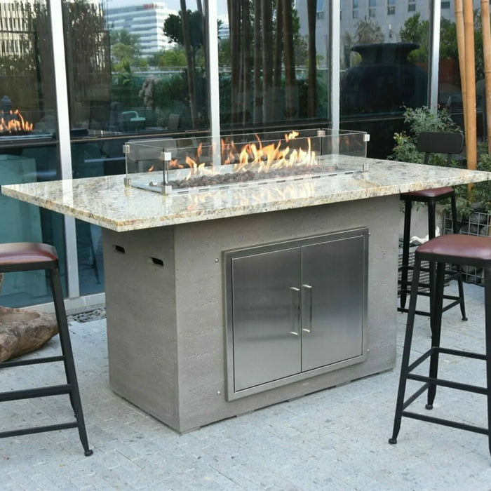 elementi bar height fire pit table that has a luxury marble counter top and is a rectangle fire pit table. the fire table is lit with a rectangular wind shield over it protecting the flame. It also have bar chairs surrounding it