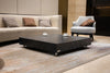 A square black marble porcelain coffee table with two cups on it in a living room setting.