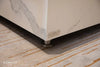 Close-up of the Elementi logo and a silver foot on a white marble porcelain coffee table.