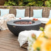 round fire pit bowl in patio in the  middle of furniture with fruit platter and glasses on the side