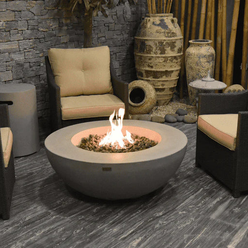 round fire pit table lit on lava rocks in between furniture