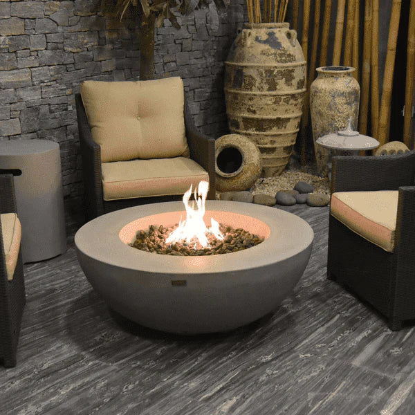 round fire pit table lit on lava rocks in between furniture