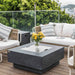 stainless steel fire table lid placed on top of square fire pit with a vase and flowers on top