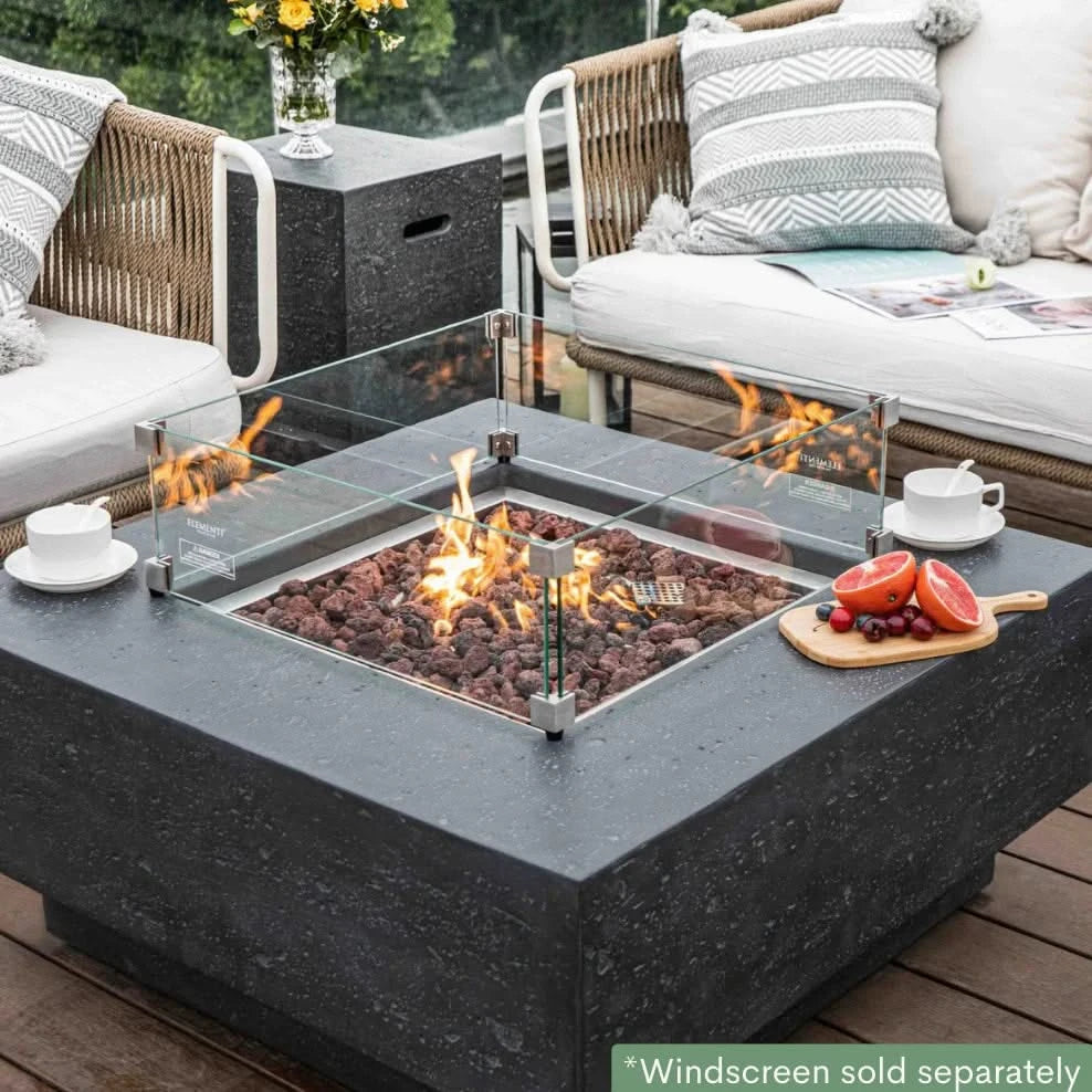dark grey square fire pit table with fruit platter and coffee cups on table. fire pit is lit on brown lava rocks and square glass windscreen