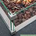 square fire pit table with glass windscreen and brown lava rocks close up