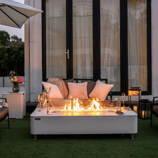 rectangle fire pit table with glass guard. fire pit is lit with orange and yellow flames. wine glasses are placed on top of fire pit table