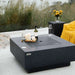 dark grey fire pit table with  fire pit lid on top. wine, wine glass and candles are on top of fire pit table