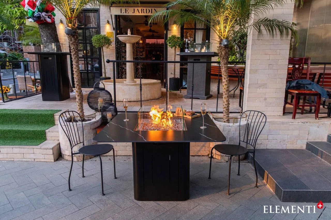 Elementi fire table with flames, wine glasses, and chairs on a restaurant patio.