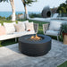 round propane fire pit table elementi plus. fire pit is lit and burning yellow and orange flames on fire glass. round fire pit in outdoor patio on top of grass and rug in between outdoor furniture