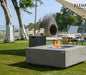 light grey square fire pit table with fire pit lit on blue fire glass in outdoor garden