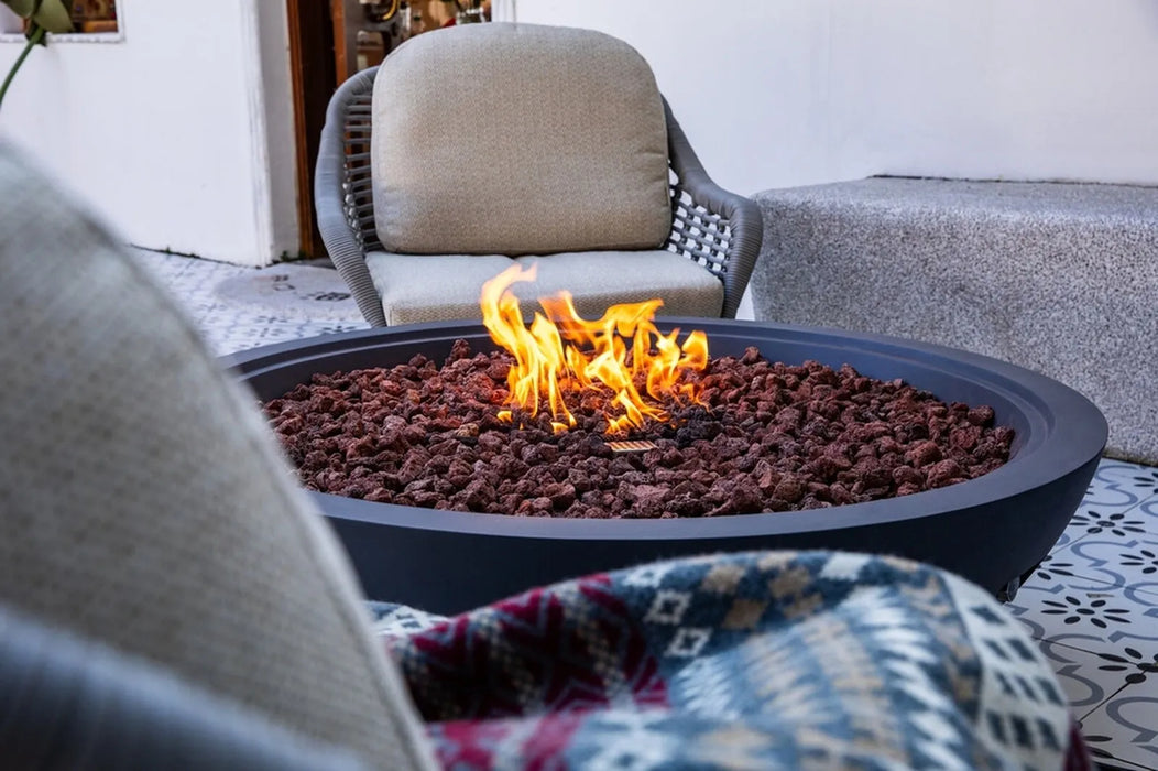 Fire pit with flames in an outdoor setting with chairs and a blanket.