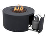 A dark gray, round fire pit table with flames burning in the center. A propane tank is visible through a sliding door on the side of the table.