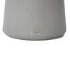 A close-up shot focuses on the base of a round, light grey object, likely the pedestal of a table. The base has a smooth, slightly textured surface and a gently curved form that widens towards the top.